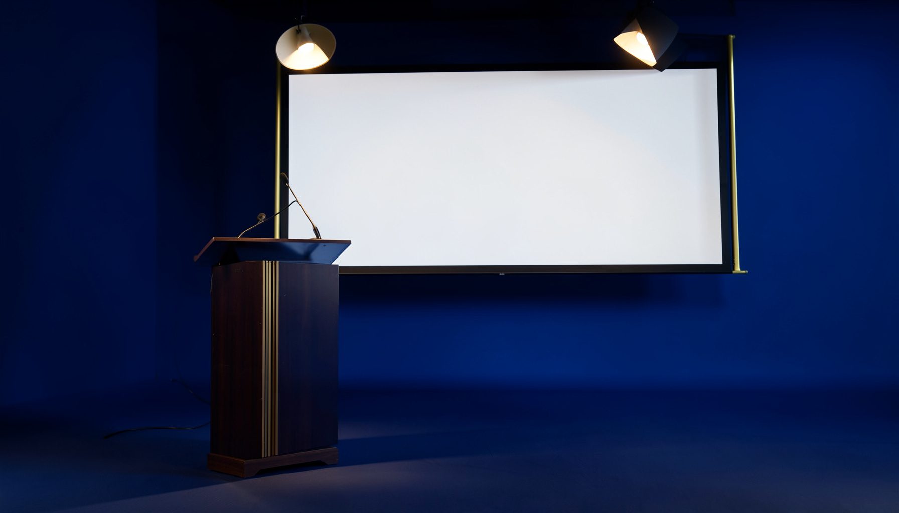 A clean, academic conference setting in deep navy and soft gold tones, featuring a podium and a large projection screen in an empty lecture hall
